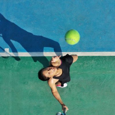 a-young-adult-woman-tennis-player-throws-ball-into-air-for-serve-casting-a-shadow-on-court-.jpg
